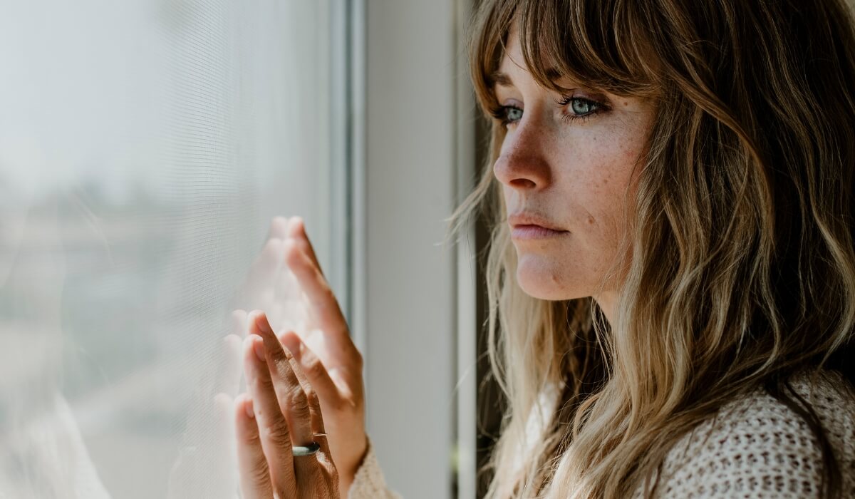 A sad woman looks out the window reflecting isolation felt during infertility depression. Image used by Get Reconnected Psychotherapy Services. Contact info@getreconnected.ca.