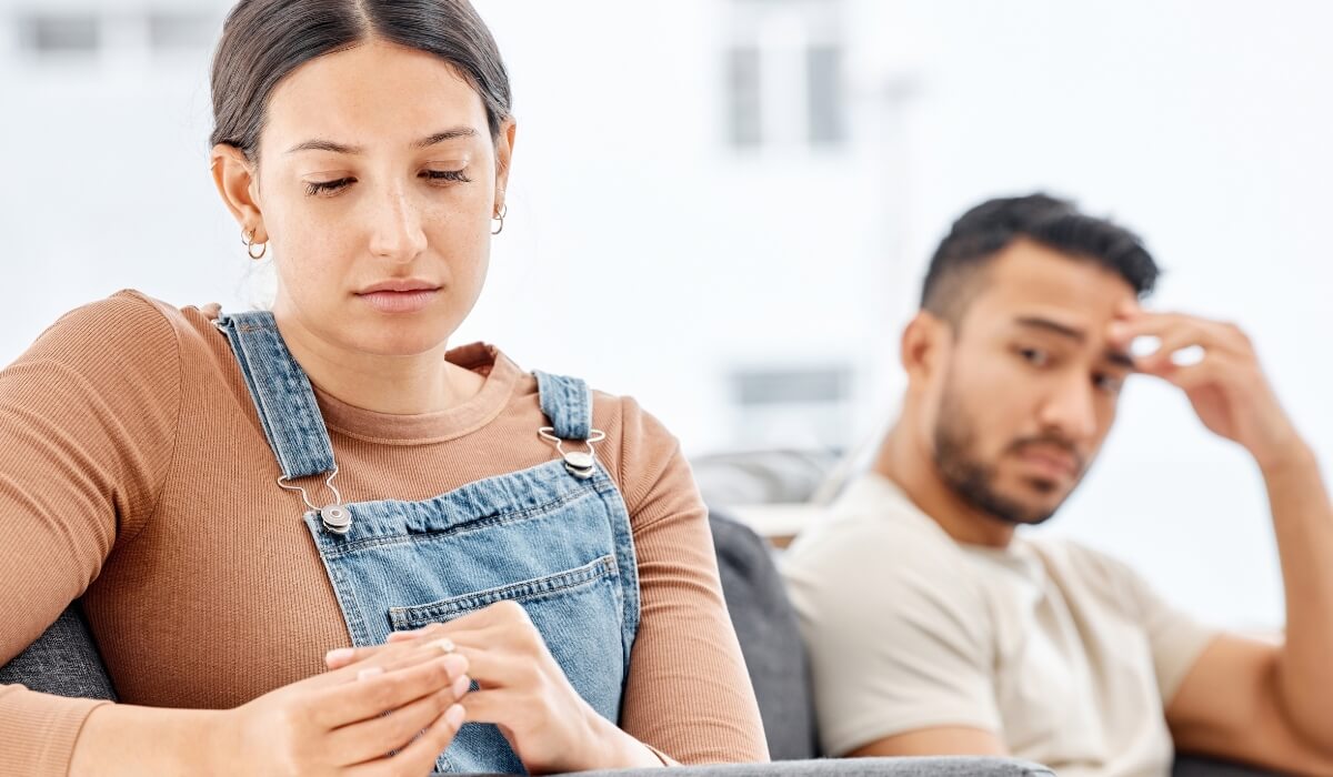 A distressed woman sits apart from her partner reflecting emotional strain linked to infertility. 
